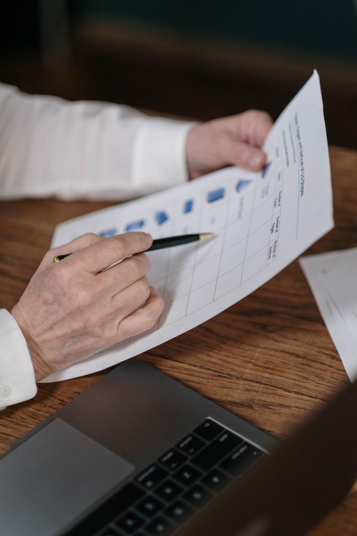 Service Senior businessperson reviews financial charts at a wooden desk, using a pen to make notes.